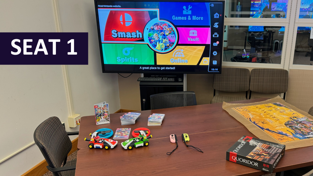 A table with Switch console controllers and Switch games. In the background is a monitor displaying a game. Floating text on image displays "Seat 1."