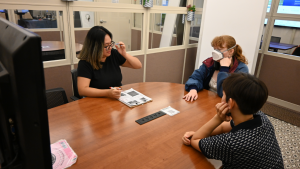 A group of students gathered in an innovator design room, which consists of a circular table, tv monitor, whiteboard, and a few chairs.