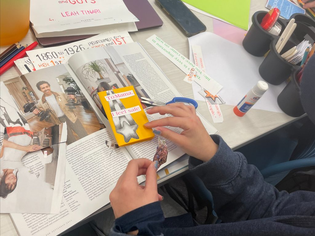 Student glues cut-outs to a zine with magazines, glue, and scissors in the background.