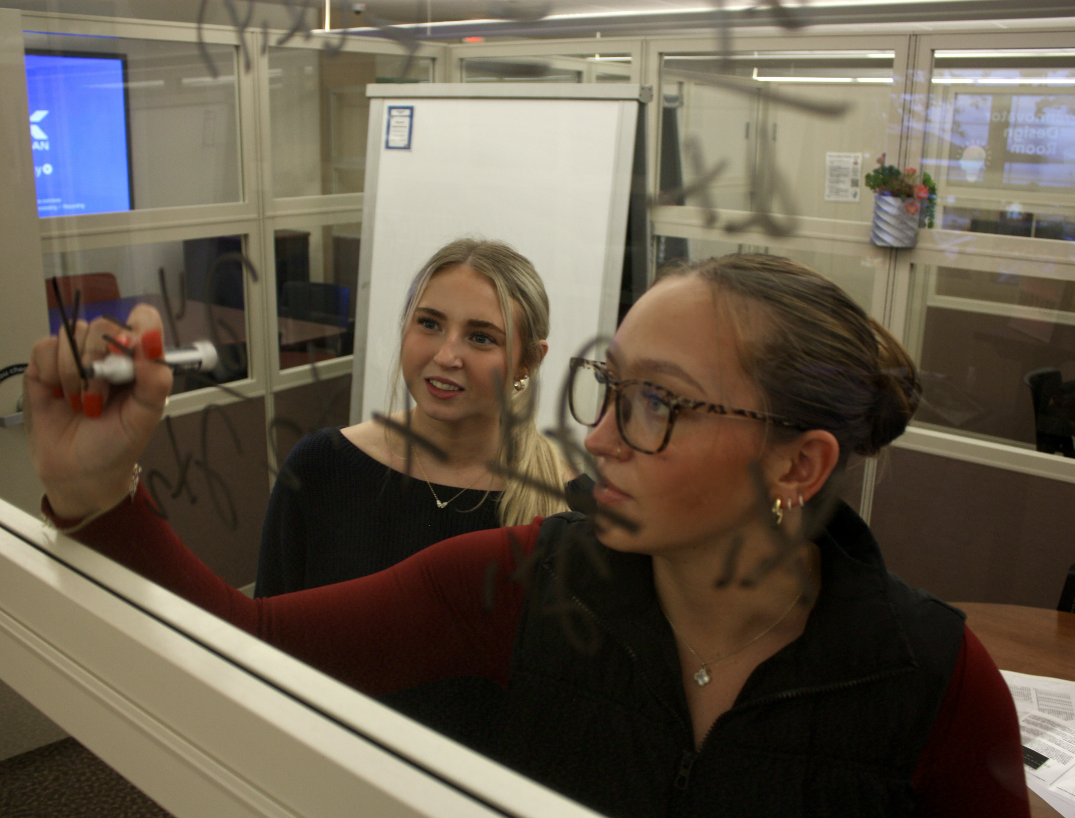 Two students use the window of an IDEA Lab reservable room as a whiteboard