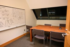 A group with chairs around a table. A window is on the slanted wall. There is a whiteboard with anatomy information written on it.
