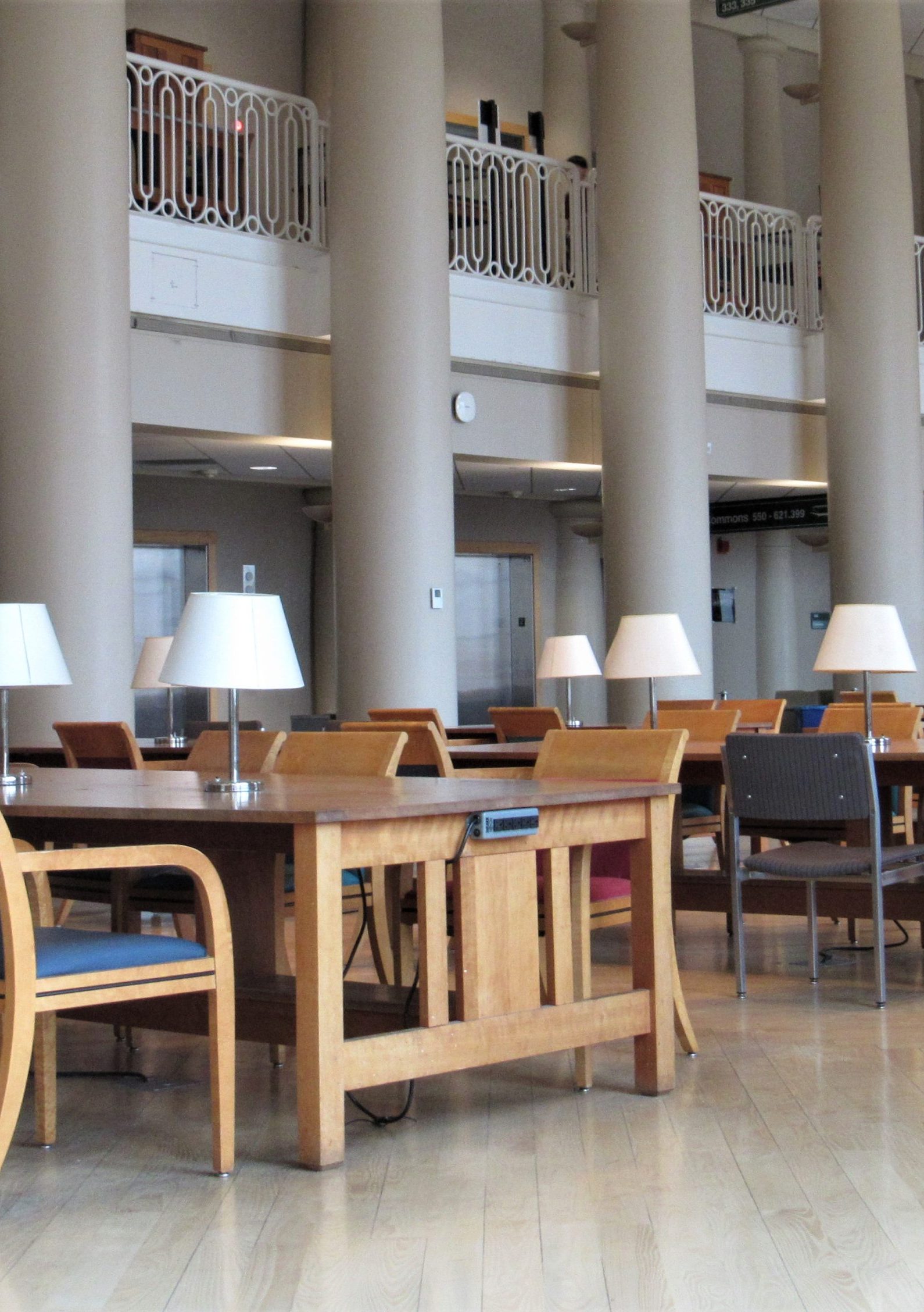 Quiet library reading space at Grainger Library with long wooden tables, chairs, and desk lamps arranged in rows beneath tall columns and an upper-level balcony.