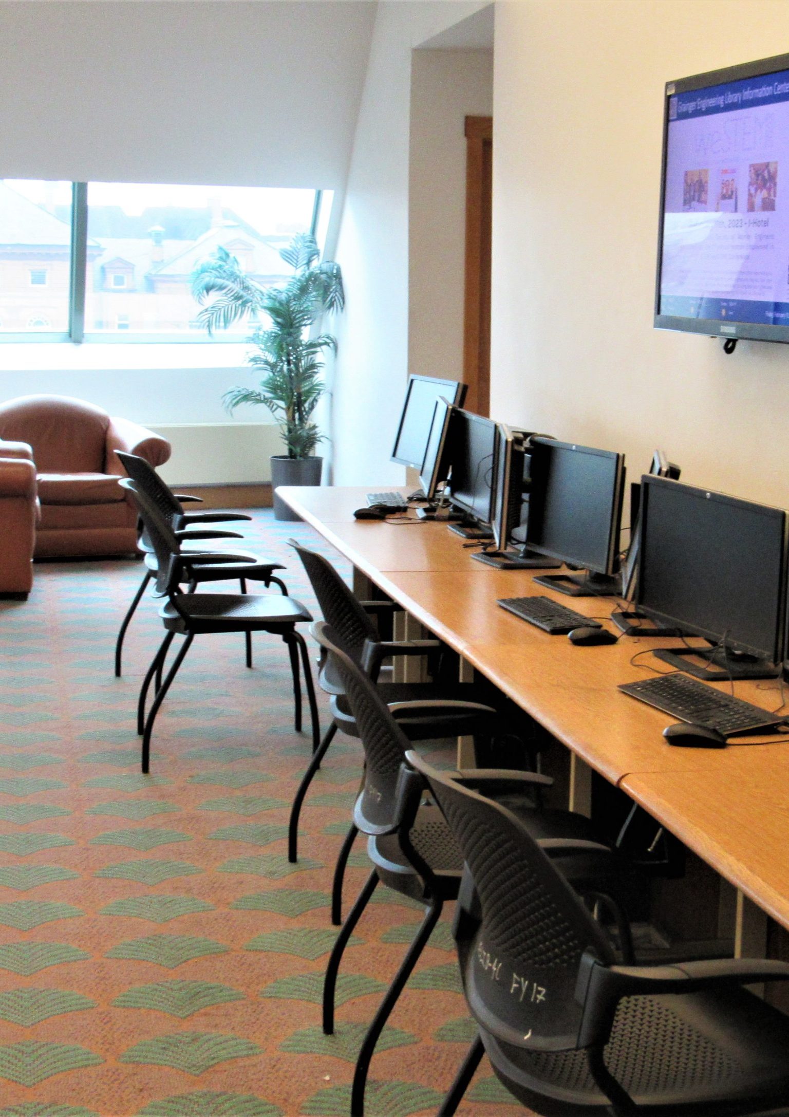 Study space at the fourth floor of Grainger library with desktop workstations and chairs with a table, and a seating area with couches near windows.