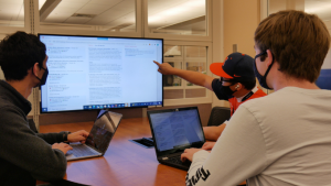 Three people working on their laptops while using the Innovator Design Room monitor.