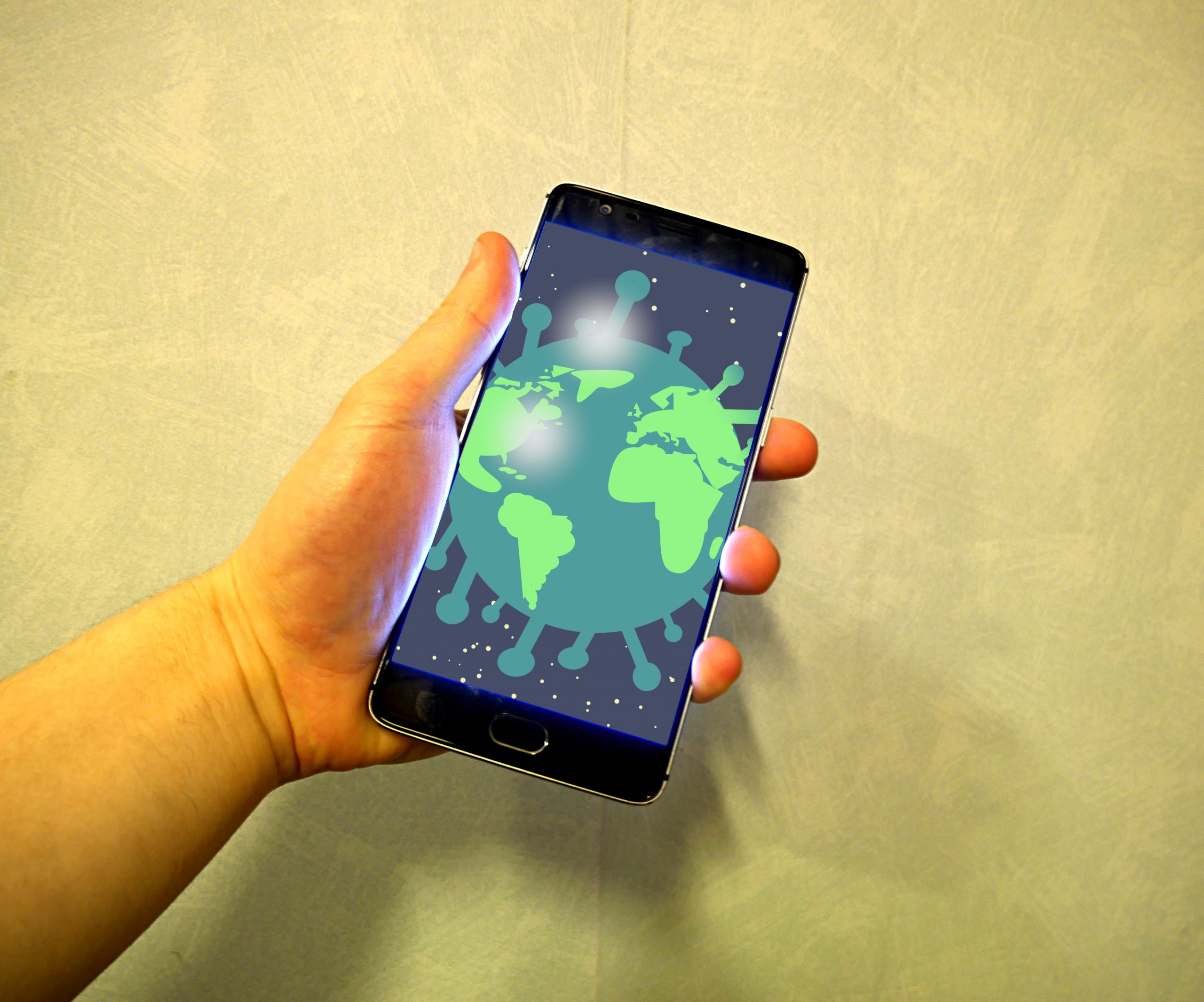 A hand holding a smartphone. The phone is showing a cartoon of the earth that has spikes like the COVID-19 virus.