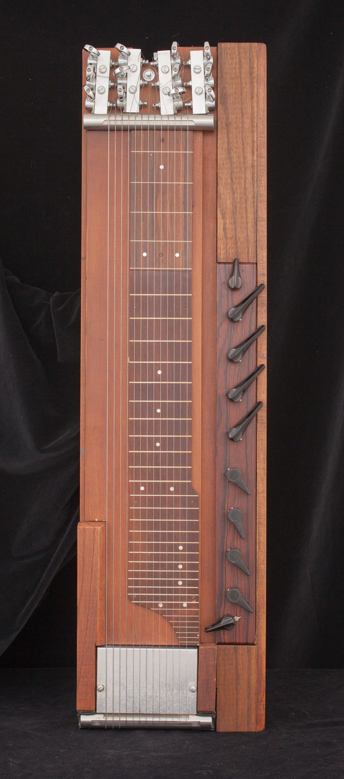 Rectangular experimental guitar made of wood. Right side has 10 levers, there are 12 strings in the center, and a metal plate at the bottom.