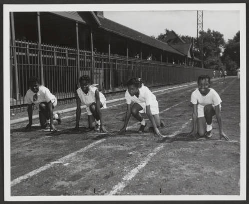 Four young women pose on a running track poised to start a sprint