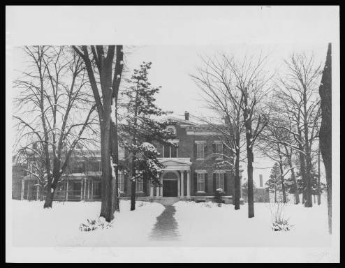 Two-story brick home with snow-covered yard in trees in the foreground