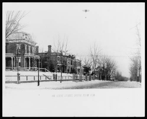 Bkack and white photograph of a snowy street next to multi-story houses