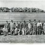 Group of coal miners pose for a photo in front of a train car loaded with coal
