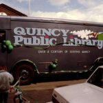 Quincy Public Library BookMobile decked out in St. Patrick's Day-themed green balloons and ribbons. Text on the side of the bookmobile reads Quincy Public Library:Over a Century of Serving Quincy