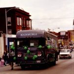 The Quincy Public Library bookmobile drives through the streets of Quincy during a pre-1991 St. Patrick's Day Parade, decked out in green balloons and ribbons