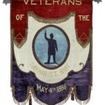 Banner made of red velvet, white taffeta and blue velvet arranged in three descending sections. Center white section has painted blue oval featuring a statue of policeman whose right arm is raised. Gold lettering reads "Veterans of the Haymarket Riot May 4th 1886." Red and blue sections are bordered with gilt fringe and tassels. Hung from a tin rod with six pointed stars on either end.