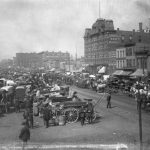 View of the Randolph Street Haymarket Square in 1886. Horse-drawn carriages line a narrow dirt street between rows of brick buildings