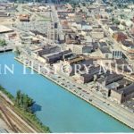 Aerial color photo of downtown Elgin. The Fox River runs through the city, next to riverfront development.