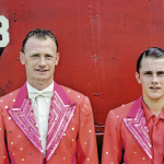 Man and son, standing side-by-side, dressed in bright pink and orange suits with rhinestones look into the camera