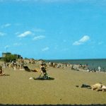 Postcard picturing sunbathers lying on a beach while people in the background wade in the shallows