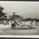 Black and white photo of a playground with children on a merry-go-round