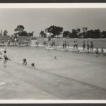 Black and white photo of a swimming pool with several people gathered around the water.