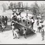 Black and white photo of several children playing on a piece of playground equipment shaped like a ringed planet