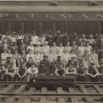Black and white photograph showing employees gathered in front of a Pullman heavy-weight car on tracks with a model car named "Spirit of Safety" in front on them on tracks
