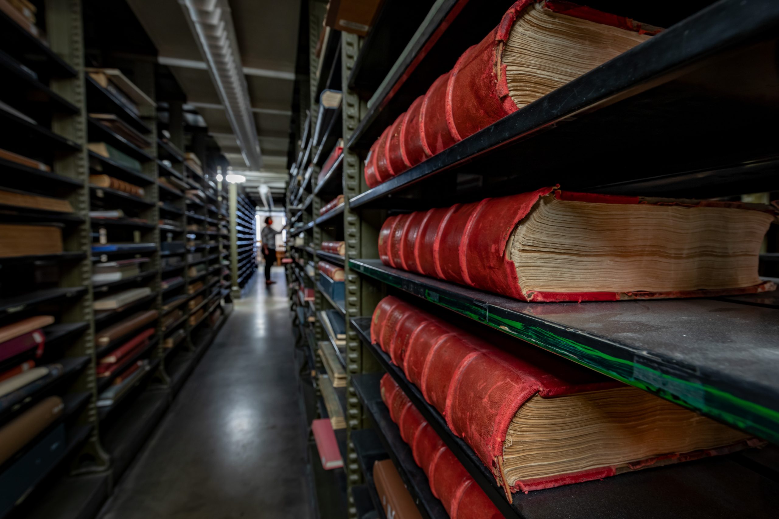 Main stacks in the Library with bookcases and person in distance.