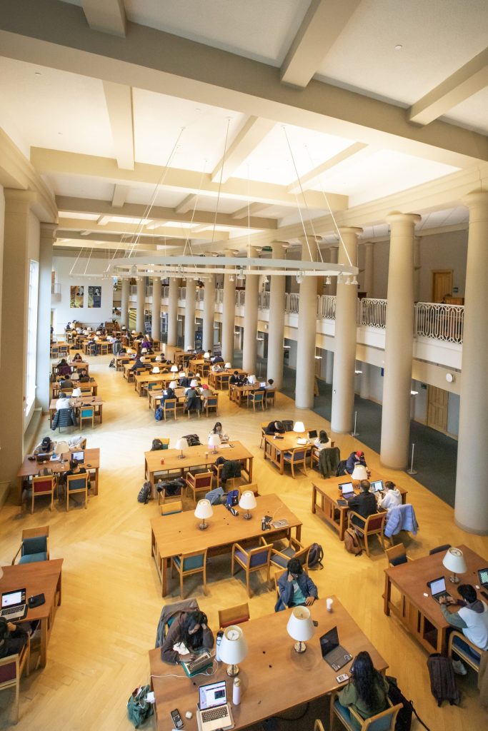 Atrium style study space in Grainger Engineering Library with large windows, natural lighting, and wooden tables.