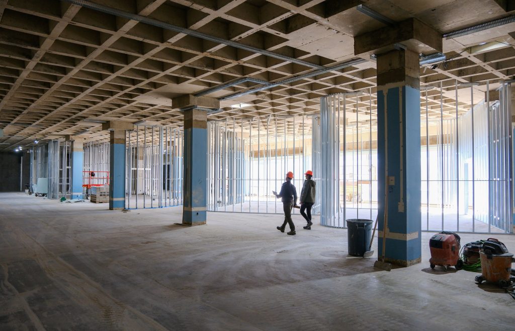 Two people wearing hard hats walk through the Archives and Special Collections Building construction site.