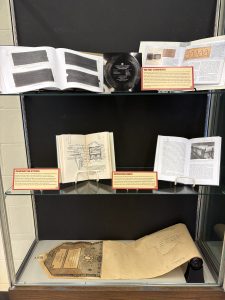 Vertical exhibit case featuring books, recordings, and a piano rolls. Items in this case discuss the first soundwaves, Enlightenment era attitudes towards recordings, and reproducing player pianos. 